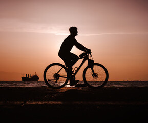 Fototapeta na wymiar Silhouette of man riding bicycle along the coastal road during the sunset.