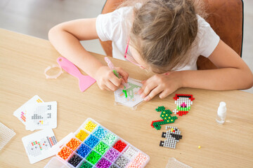 A girl sitting at a table makes figures out of colorful beads. Aqua mosaic game. The concept of...