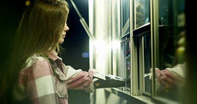 close-up of a long-haired woman with a bionic hand who pays for a purchase at a kiosk in the park using a debit card. everyday life and socialization of disabled people who have received new