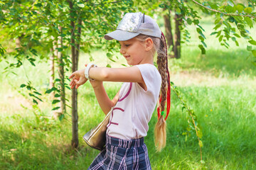 Child schooler using smartwatch outdoor park. Kid talking on vdeo call with parents on smartwatches. Schoolgirl searching on the internet using watches touchscreen display.Smart wristwatch GPS tracker