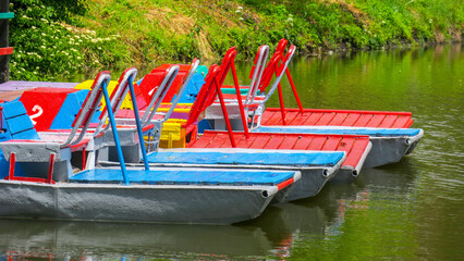 Colored metal catamarans are moored to the shore in the park