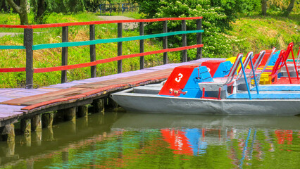 Colored metal catamarans are moored to the shore in the park