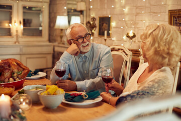 Happy senior couple drink wine and talk during Thanksgiving dinner at home.