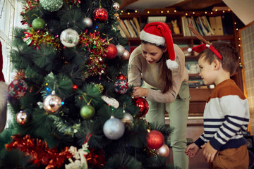 Happy mother and son decorate Christmas tree together at home.