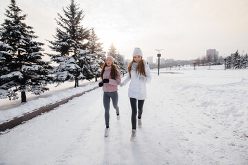 Fototapeta na wymiar Two young athletic girls running in the park on a sunny winter day. A healthy way of life.