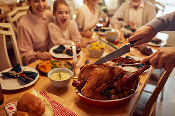 Close-up of man carves Thanksgiving turkey during family dinner at dining table.