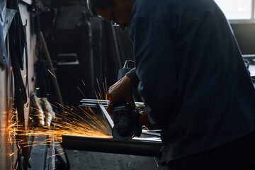Side view of industrial worker in overalls grinding welded metal and polishing steel with sparks....