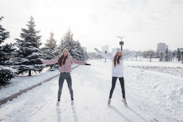 Two young athletic girls do a warm-up before running on a sunny winter day. A healthy way of life.