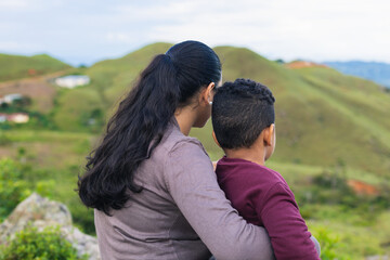 woman sitting on the rocks looking at the landscape with her son, embraced
