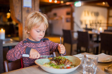 Preschool child, cute boy, eating lamb meat in a restaurant, cozy atmosphere, local small restaurant in Tromso, Norway