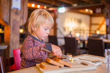 Fototapeta na wymiar Preschool child, cute boy, eating bread in a restaurant, cozy atmosphere, local small restaurant in Tromso, Norway