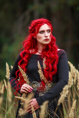 Courageous young lady with long red hair in image of fabulous historical character of witch and priestess in a mystical forest