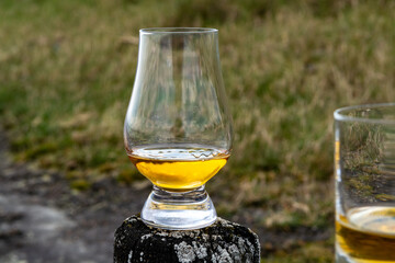 Tasting of dram single malt scotch whisky on seashore in Scotland, old wooden pole with whisky glass