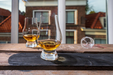 Dram of single malt scotch whisky served in tasting glass with view on old window and houses