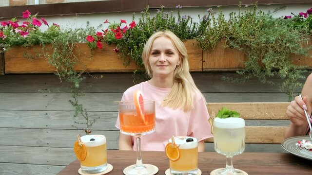 Blondy young woman chooses and drinks a cocktail in a glass.