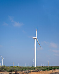 Tall Windmills distributed in an open field with nice, clear blue sky background.