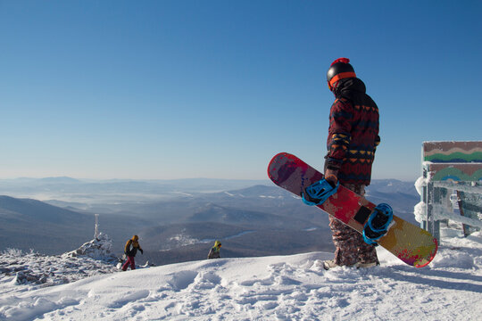 A man in snowboarding gear on the top of a mountain. Young man standing with a snowboard on the top of the mountains