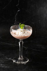 Glass of ice cold Baileys cocktail served in a coupe glass, decorated with mint leaf placed on a black background