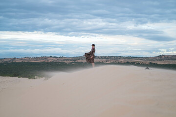 Wanderer walking in the desert. Young man standing in white sand dunes. Stranger in desert. Sand flies in the wind. Clothes fluttering in the wind