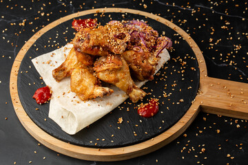baked buffalo chicken wings with sesame seeds, onion and chili slices on black wooden board.