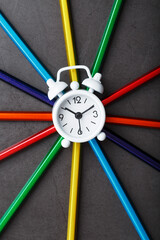 A white alarm clock with colored pencils in the shape of a star