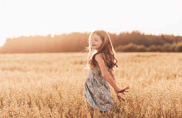 A happy little girl runs through a wheat field in the summer on a sunny day. Summertime. Summer vacation. Happy childhood. Positive emotions and energy