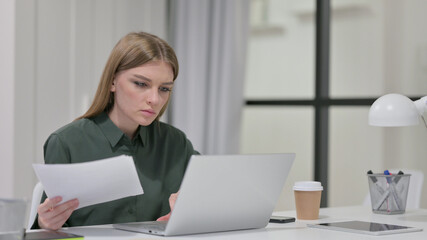 Young Woman Reading Documents while working on Laptop 