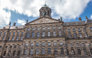 Amsterdam, Netherlands - August 14, 2021: Closeup of front brown stone facade and monumental gable and clock tower of Royal Palace under blue cloudscape. 