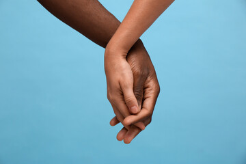 Woman and African American man holding hands on light blue background, closeup - Powered by Adobe