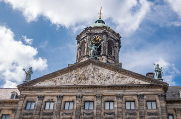 Fototapeta na wymiar Amsterdam, Netherlands - August 14, 2021: Closeup of front brown stone monumental gable and clock tower of Royal Palace under blue cloudscape. Dense fresco and bronze statues.