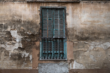 Fototapeta na wymiar old rustic shutter of a balcony door in south Europe, in a bluish color tone. walls of the vintage house with different structure and colors 