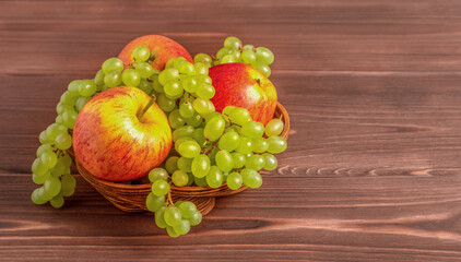 Grapes and apples in a wooden basket on a wooden table. Copy space.
