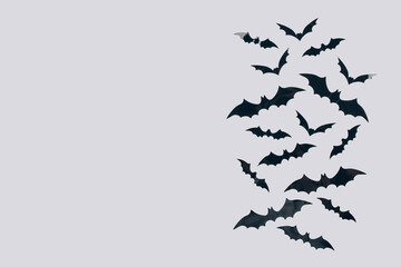 Halloween background - decorative black paper bats on light gray background with copy space for text. Halloween decorations or party invitation concept. Selective focus