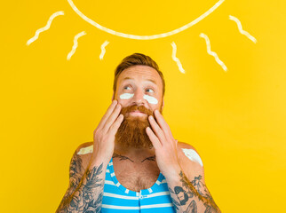 Man with tattoos and swimsuit puts on sunscreen