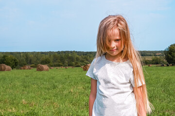 Little girl with long blonde hair in a field with hay rolls