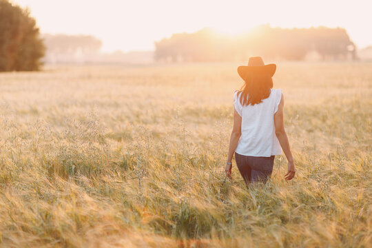 Woman farmer in cowboy hat walking at agricultural field on sunset. Labor day concept