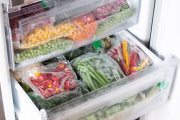 Plastic bags with different frozen vegetables in refrigerator.
