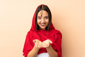 Young Indian woman isolated on beige background holding copyspace imaginary on the palm to insert an ad