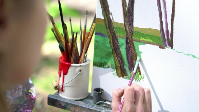 Artist at the plein air painting. An oil painting on the canvas in the park. Creative summer mood.