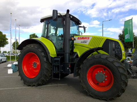 New tractor CLAAS Axion 820 in agricultural machinery exhibition. Venue for farmers business. Manufacturing equipment for crop production. Red wheel disk.