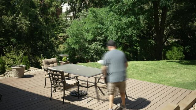 A time lapse view of a man setting up his backyard deck furniture.	