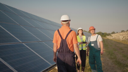 An employee of a solar power plant talks on a walkie-talkie while his colleagues and an investor check the solar power plant with an infrared scanner, a drone. Photovoltaic solar panel installation