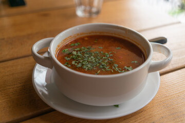 Kharcho soup with parsley in a white bowl on a wooden table in a restaurant