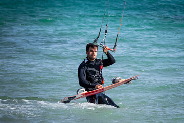 Young mediterranean man sets out to kitesurf. He is in the water with a black wetsuit and about to fly the kite.