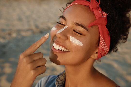 Happy African American woman with sun protection cream on face at beach, closeup