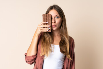 Young Lithuanian woman isolated on beige background taking a chocolate tablet and surprised
