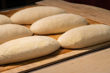 Several loaves of raw dough lie on a wooden board. Craft bread before baking