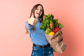 Young Lithuanian woman holding a grocery shopping bag with thumbs up because something good has happened