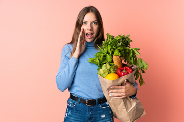 Young Lithuanian woman holding a grocery shopping bag with surprise and shocked facial expression