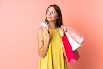 Young Lithuanian woman isolated on pink background holding shopping bags and a credit card and thinking
